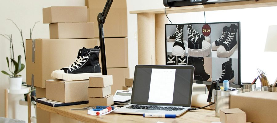 A busy workspace with sneakers, boxes, and a laptop indicating an online shoe store or e-commerce setup.